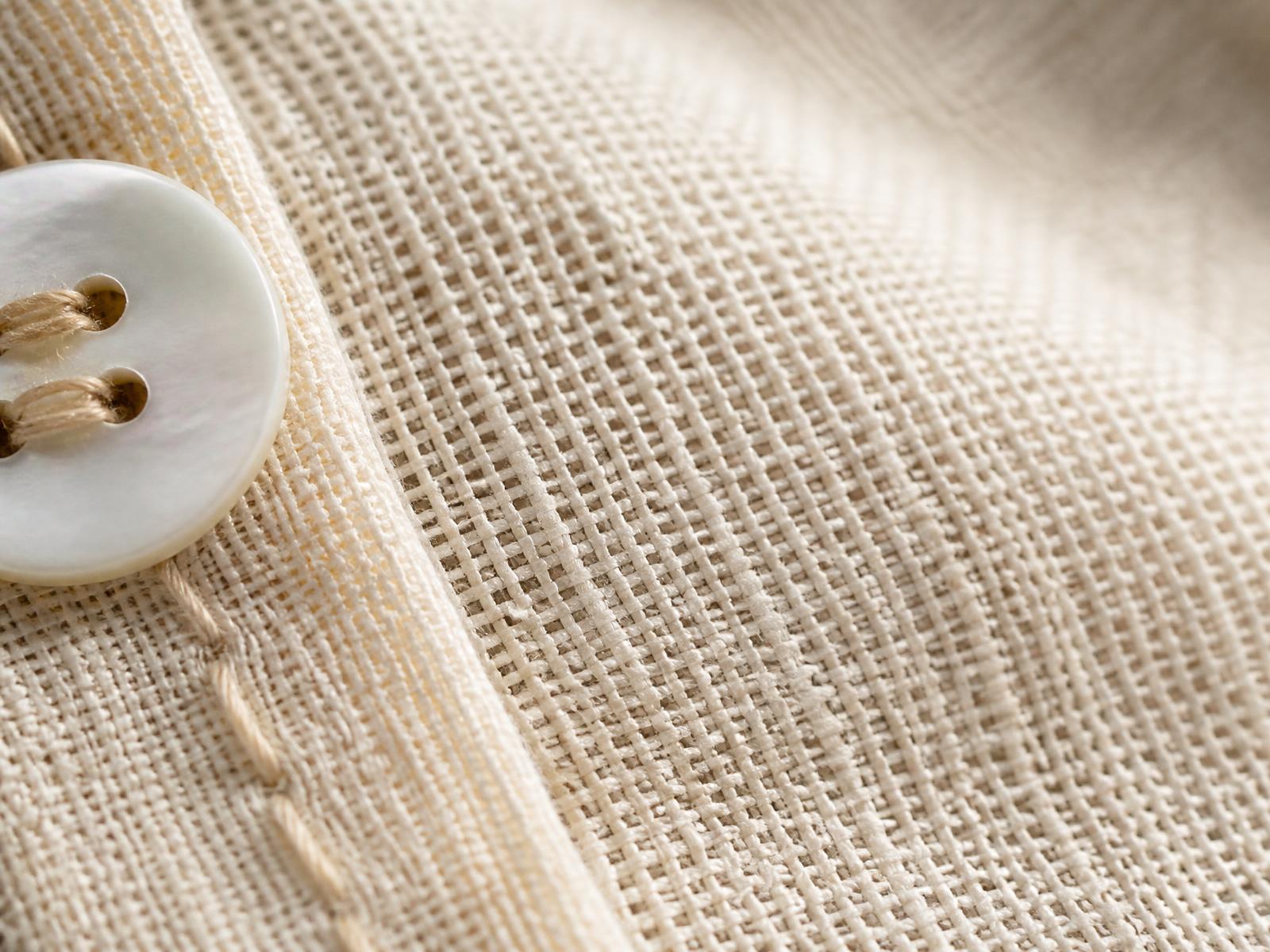 Macro detail of the fine open weave, hand stitching and shell button